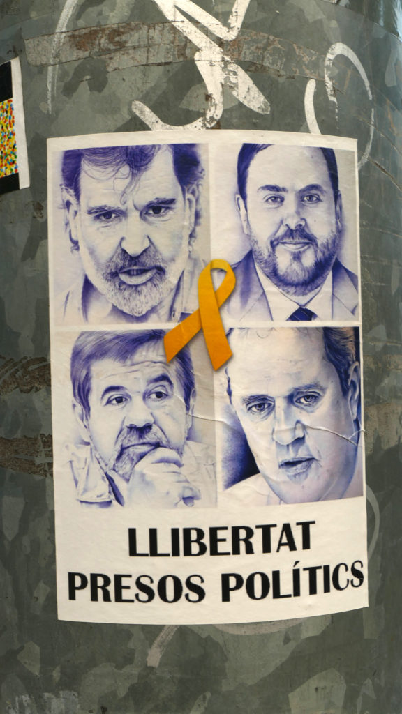 "Vrijheid voor de politieke gevangenen", poster met vier portretten en een gele strik (symbool van de oproep tot veilige terugkeer van de vervolgden). Jordi Cuixart (linksboven), Oriol Junqueras (rechtsboven), Jordi Sànchez (linksonder), Joaquim Forn. Foto ©2018 Huib J. Lirb 